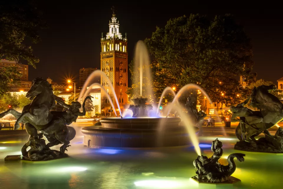 Nighttime shot of decorative fountain with horses and Country Club Plaza tower in background